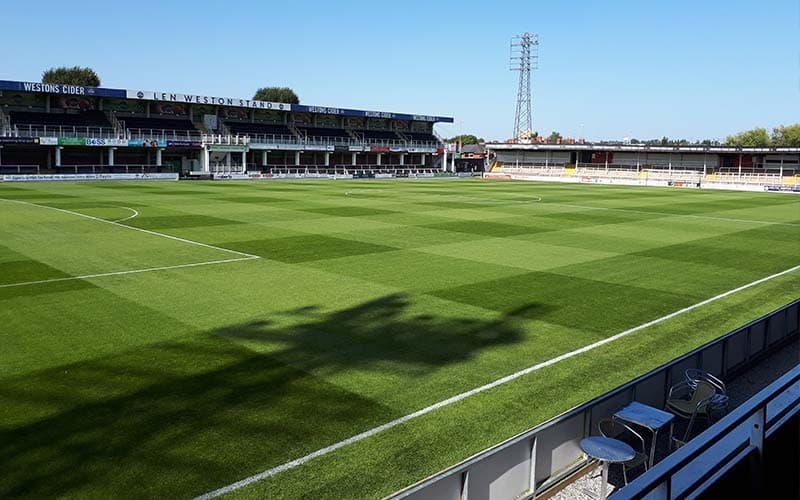 An empty football pitch and empty stands on a sunny day.