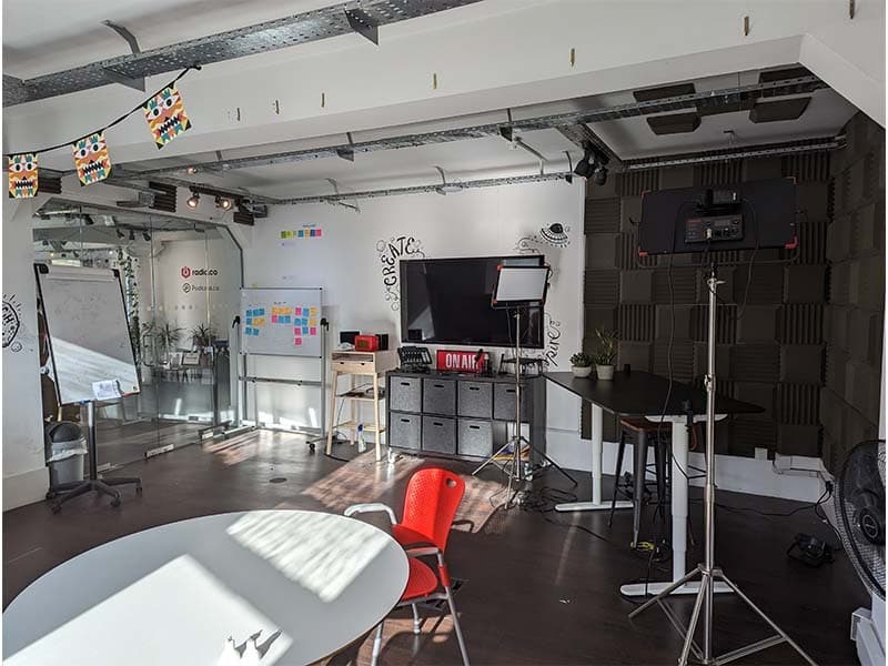 Image shows an office space with wooden flooring, desks, and there are some acoustic panels in the right hand corner.