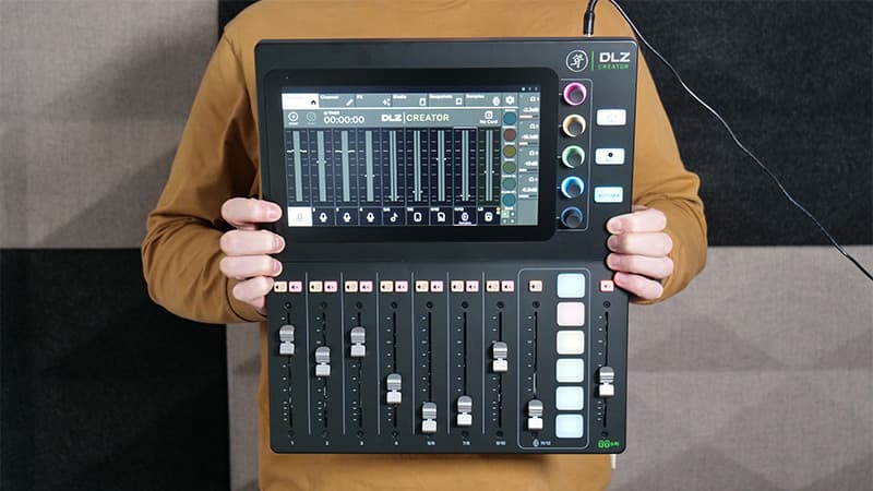 A person holding up the Mackie DLZ Creator mixer, against a black and white background.