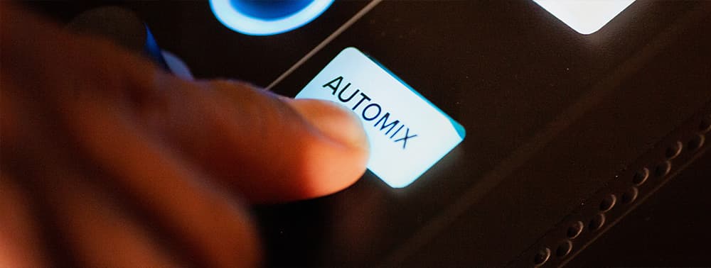 A close-up of a finger pushing the automix button on the Mackie DLZ Creator mixer.