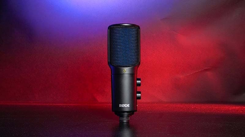 The RODE NT-USB+ mic, positioned upright on a table. Illuminated with red and blue lights.