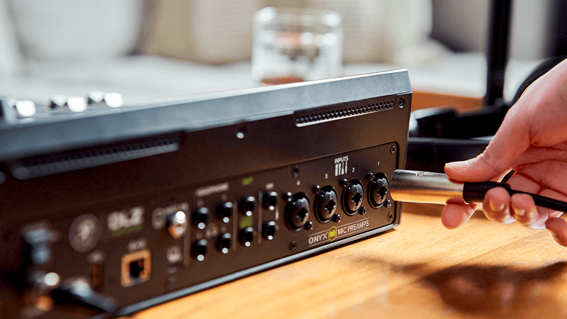A hand plugging in an XLR cable in to the back of a Mackie DLZ Creator mixer.